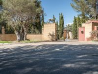 a driveway with some trees and some stone walls and a fence and gates with a statue of a horse