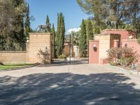 a driveway with some trees and some stone walls and a fence and gates with a statue of a horse