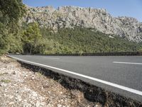 road with gravel and rocks on it in front of mountain range with blue sky and white clouds