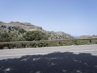 a paved road passes through the mountains near some trees, rocks and sea in the distance