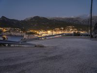 a view of a mountain landscape and the sea and town lights from above on a hillside with the road going to a city