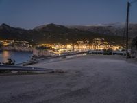 a view of a mountain landscape and the sea and town lights from above on a hillside with the road going to a city