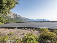 the curved road is near the mountainous mountainside with a car passing it on a clear day