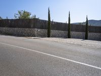 a street sign on the corner of a road near a fence and some trees and shrubs