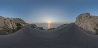 a skateboarder on a paved road surrounded by mountains and ocean waves at sunrise