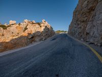 the road is covered in gravel along side cliffs and boulders with blue sky behind it