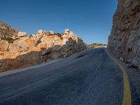 the road is covered in gravel along side cliffs and boulders with blue sky behind it