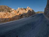 the road is covered in gravel along side cliffs and boulders with blue sky behind it