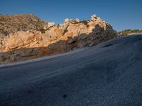 the road is covered in gravel along side cliffs and boulders with blue sky behind it