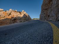 the road is covered in gravel along side cliffs and boulders with blue sky behind it