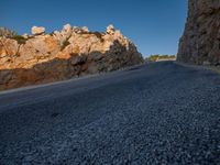 the road is covered in gravel along side cliffs and boulders with blue sky behind it