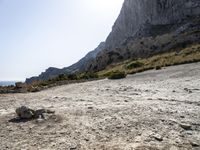 a person stands on a rocky cliff next to the ocean with some rocks and gravel below