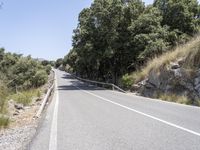 a road with trees and rocks next to the roadway by a hill top with a motorcycle on the right