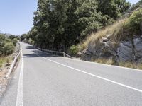 a road with trees and rocks next to the roadway by a hill top with a motorcycle on the right