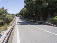 a road with trees and rocks next to the roadway by a hill top with a motorcycle on the right