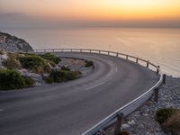 curved road with two traffic lanes at sunset overlooking the ocean and hills at sea side