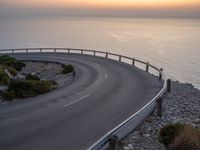 curved road with two traffic lanes at sunset overlooking the ocean and hills at sea side