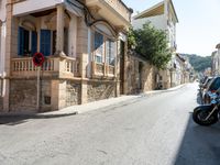 a motorcycle sits parked along a narrow road in the middle of town as people walk by