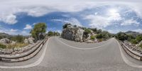 a fisheye lens shot of a winding, paved road and rock mountain range in the background