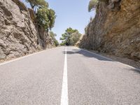 a long narrow road near large rock formations, on a sunny day with the sun shining