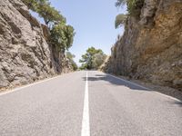 a long narrow road near large rock formations, on a sunny day with the sun shining