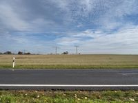 man in bicycle helmet on the road looking down at something in the distance with an empty field behind him