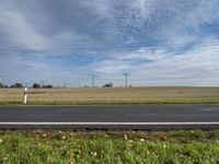 man in bicycle helmet on the road looking down at something in the distance with an empty field behind him