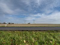 man in bicycle helmet on the road looking down at something in the distance with an empty field behind him