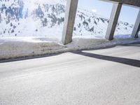 man on bike wearing all black rides through the tunnel underpass between buildings and snowy mountains