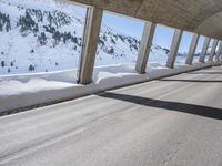 man on bike wearing all black rides through the tunnel underpass between buildings and snowy mountains