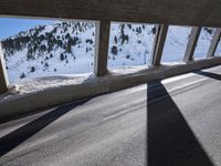 man on bike wearing all black rides through the tunnel underpass between buildings and snowy mountains