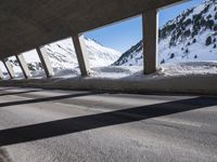 man on bike wearing all black rides through the tunnel underpass between buildings and snowy mountains