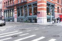 a man wearing a white shirt crossing the street in front of a red brick building