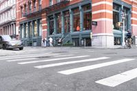 a man wearing a white shirt crossing the street in front of a red brick building