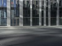 man crossing street in front of large glass building in urban area with gray pavement and street light