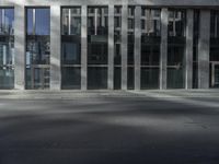 man crossing street in front of large glass building in urban area with gray pavement and street light