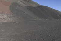 a man riding a red bicycle past a hill of rocks and gravels on a desert road