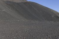 a man riding a red bicycle past a hill of rocks and gravels on a desert road