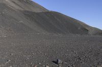 a man riding a red bicycle past a hill of rocks and gravels on a desert road