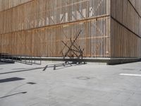 a man riding his bicycle on a concrete sidewalk outside of a building made out of wood planks