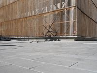 a man riding his bicycle on a concrete sidewalk outside of a building made out of wood planks