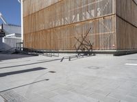 a man riding his bicycle on a concrete sidewalk outside of a building made out of wood planks