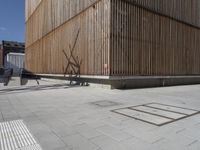 a man riding his bicycle on a concrete sidewalk outside of a building made out of wood planks