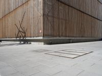 a man riding his bicycle on a concrete sidewalk outside of a building made out of wood planks