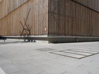 a man riding his bicycle on a concrete sidewalk outside of a building made out of wood planks