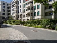 a man riding a bike down a street next to apartment building and some bushes and trees