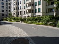 a man riding a bike down a street next to apartment building and some bushes and trees