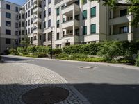 a man riding a bike down a street next to apartment building and some bushes and trees