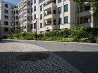 a man riding a bike down a street next to apartment building and some bushes and trees