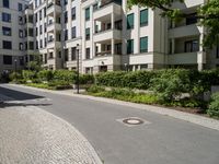 a man riding a bike down a street next to apartment building and some bushes and trees